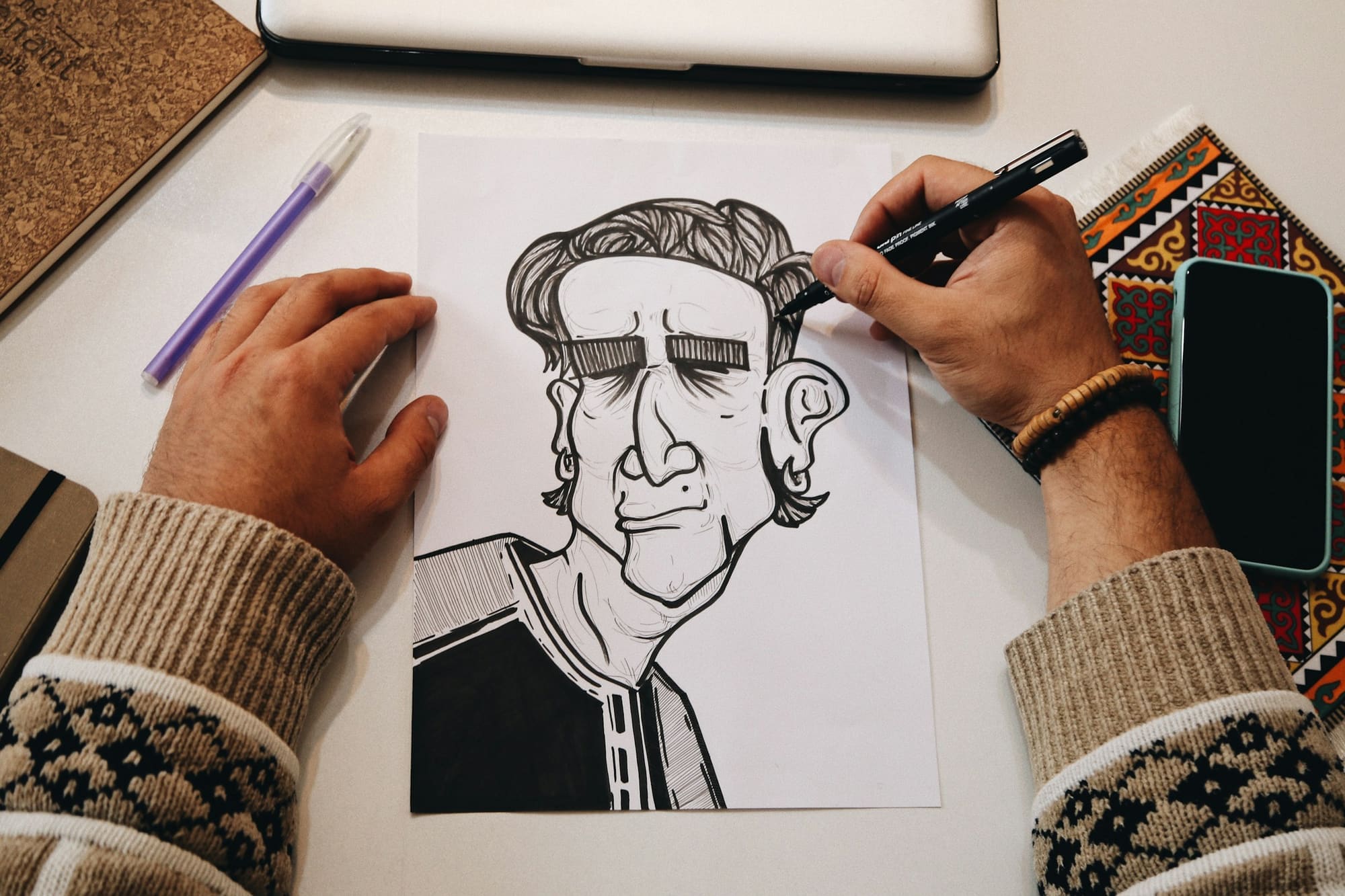 An illustrator inks a bold caricature with a black marker on white paper.