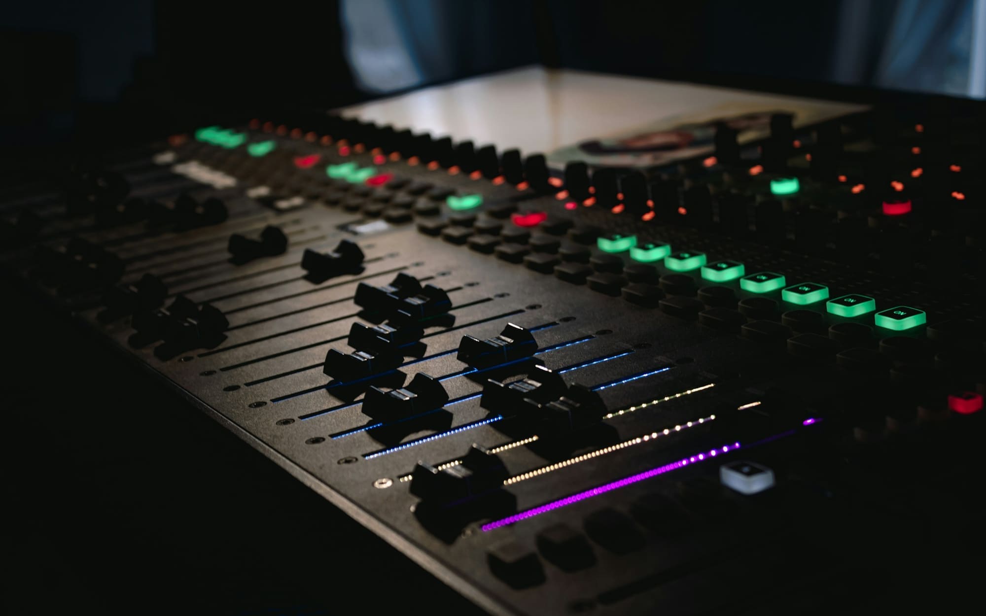 Faders and glowing channel lights on an audio mixing console in a dark studio.