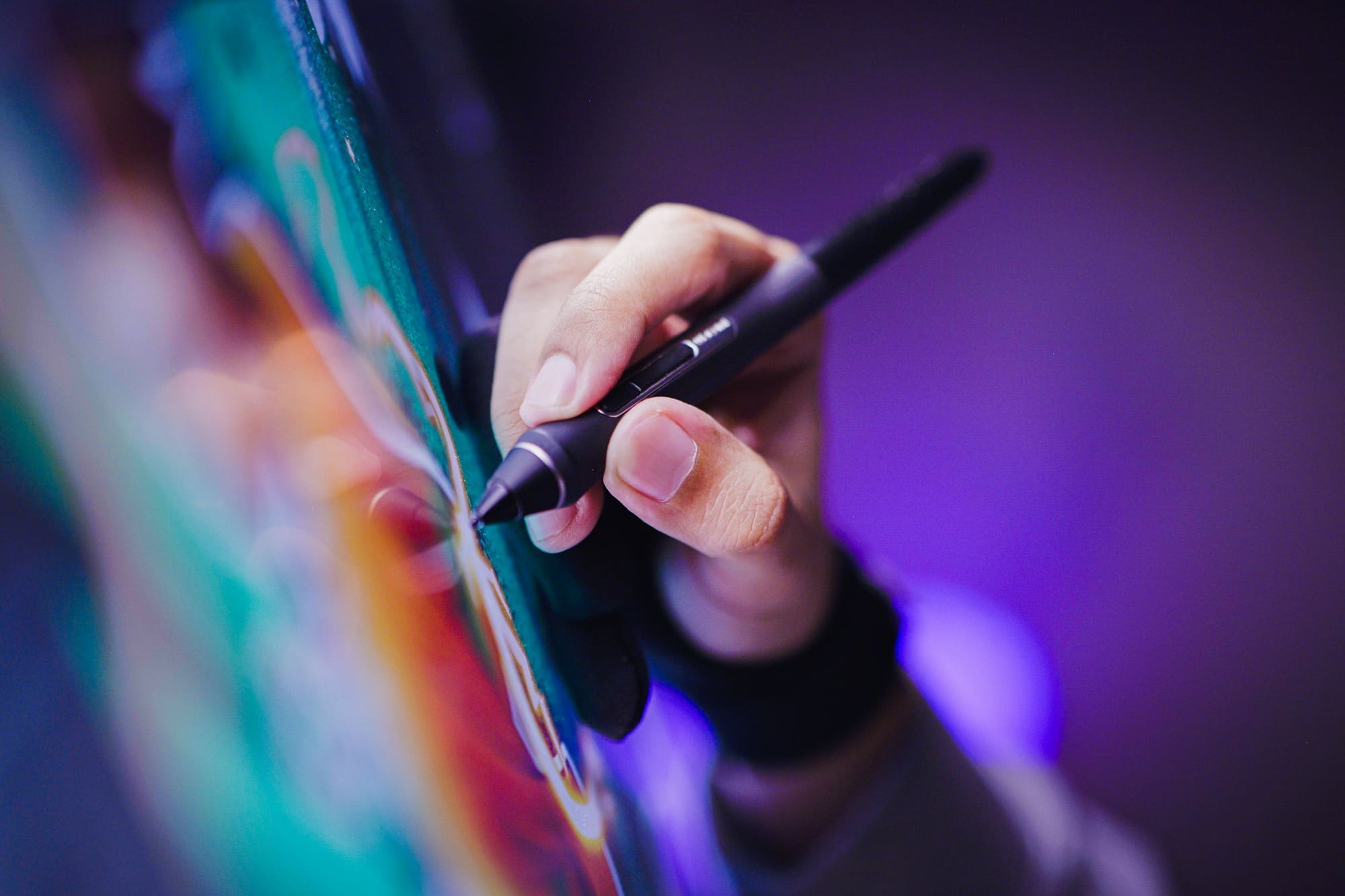 Close-up of a hand drawing with a digital pen on a colorful screen in violet light.