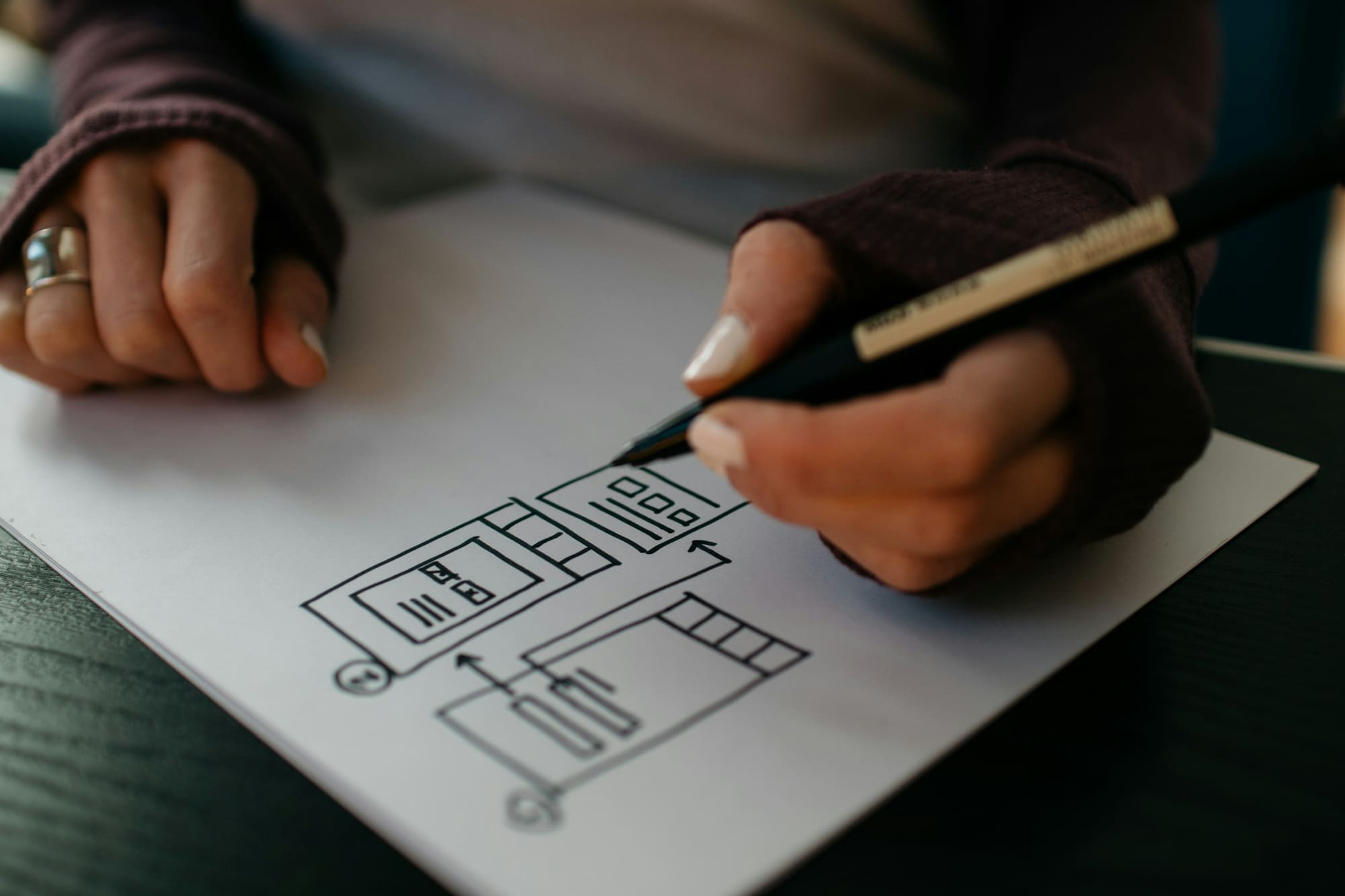 A designer sketches an app wireframe with a pen on white paper.
